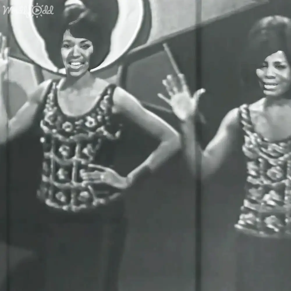 Young adult female performers on a stage with intricate patterned sleeveless tops and textured fabric under bright lighting.