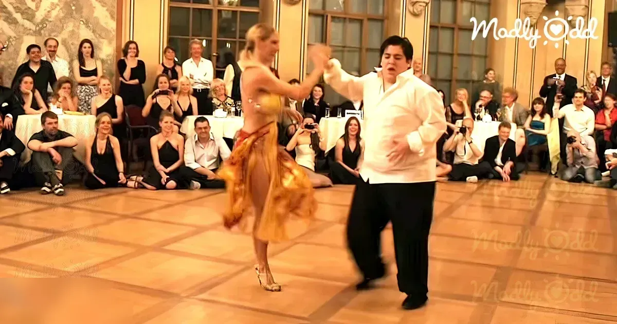 A couple dancing elegantly in a formal ballroom setting with ornate decor and warm lighting.