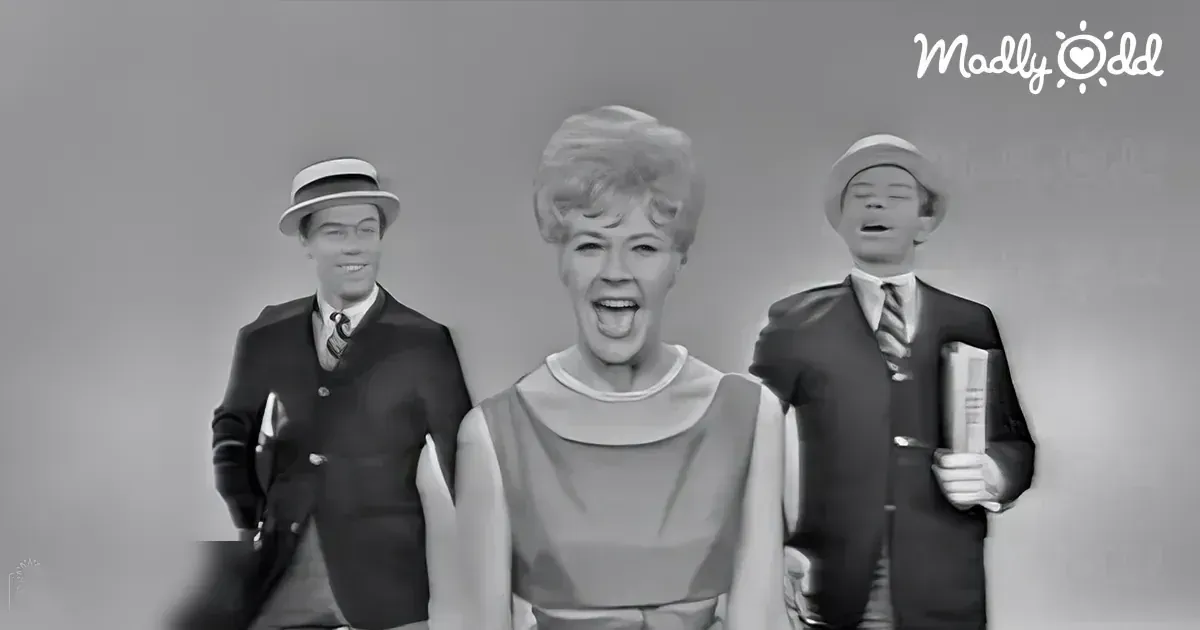 Middle-aged woman in a light-colored dress with a collar and sleeveless design, surrounded by two young adult men wearing dark suits and patterned ties, holding books against a plain white background.