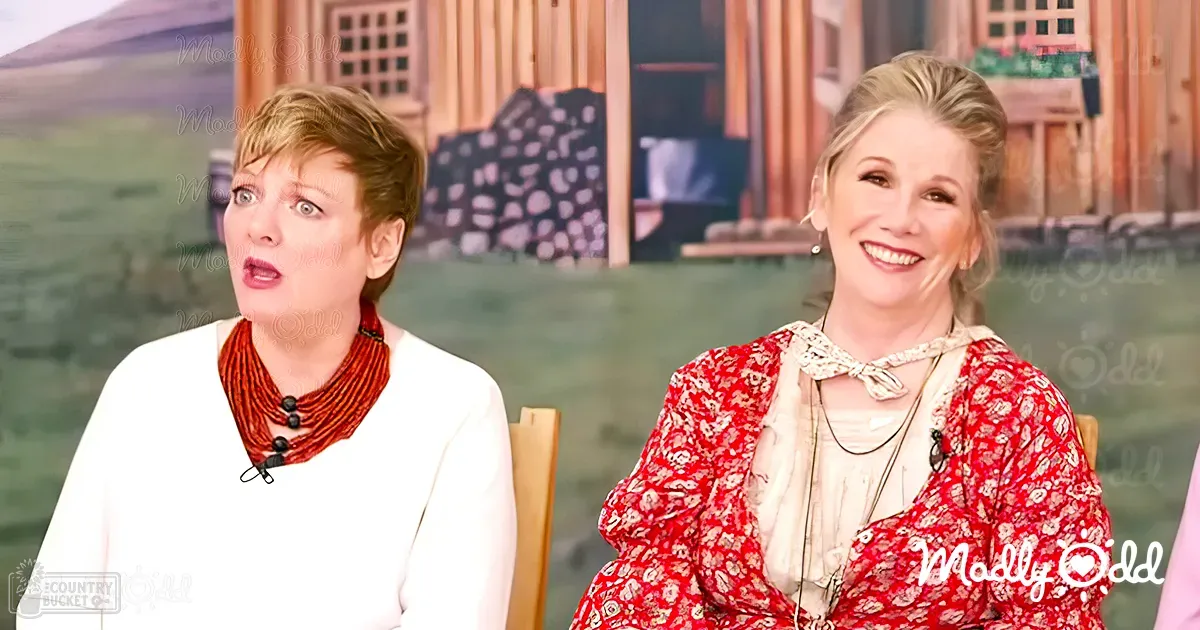 Two women in a studio setting; Person 1 wears a white long-sleeved top with a fitted cut, while Person 2 dons a red floral dress with puffed sleeves. A wooden chair and an outdoor backdrop are visible.