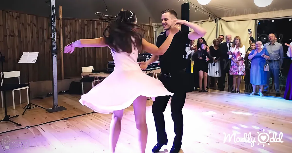 A couple dancing at an indoor wedding reception with a rustic barn-style setting, evening lighting.