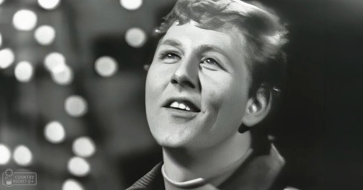 A young adult female wearing a dark-colored jacket or blazer with a high collar and short sleeves stands indoors under circular bokeh stage lighting.