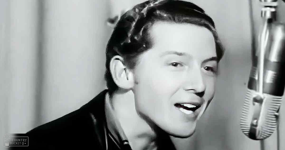 A young adult male stands in a recording studio with a vintage microphone on the right side.