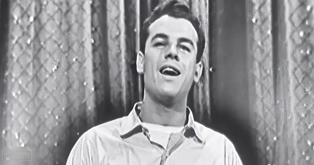 Young adult male wearing a white collared, button-down shirt with long sleeves and relaxed fit in an indoor setting with textured diamond-patterned walls.