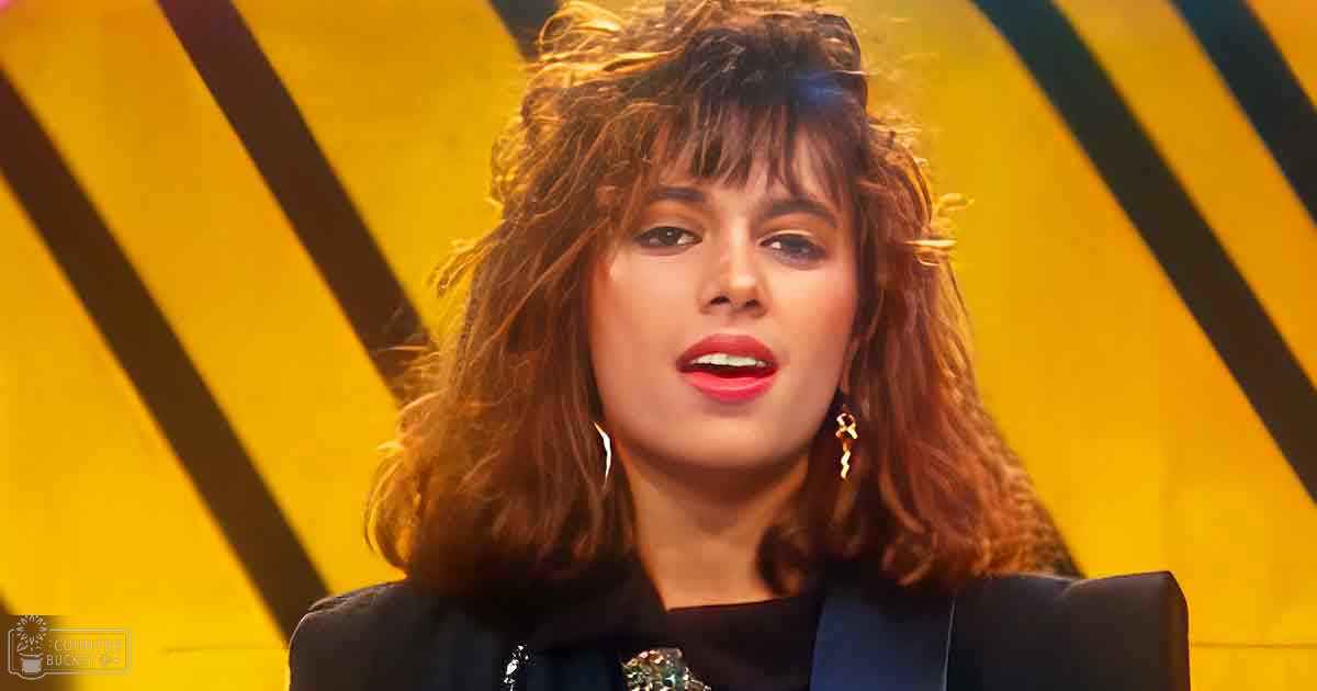A young adult female in a dark blazer with shiny brooch, gold hoop earrings, and bold striped yellow background suggests a professional or stage setting.
