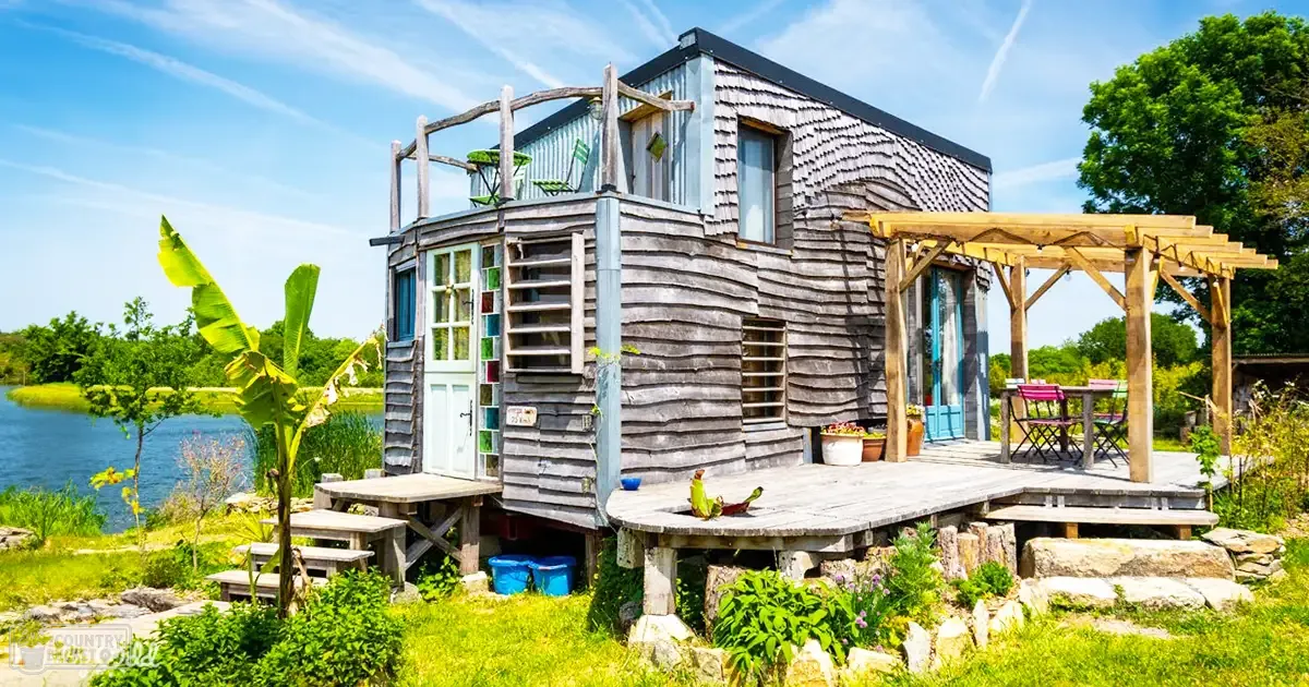 A serene cabin-like structure surrounded by lush greenery near a body of water, with vibrant spring or summer foliage and clear daytime light.