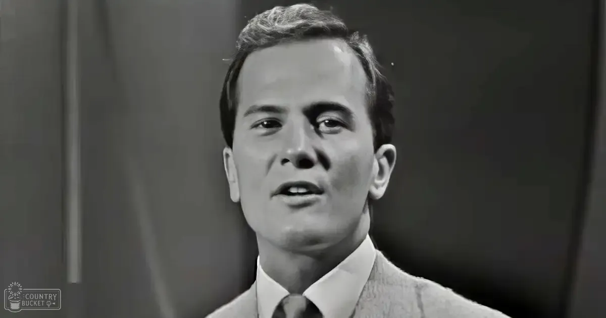 Young adult male in formal attire, light-colored suit jacket, white collared shirt, dark tie, indoor setting with neutral walls and soft lighting.