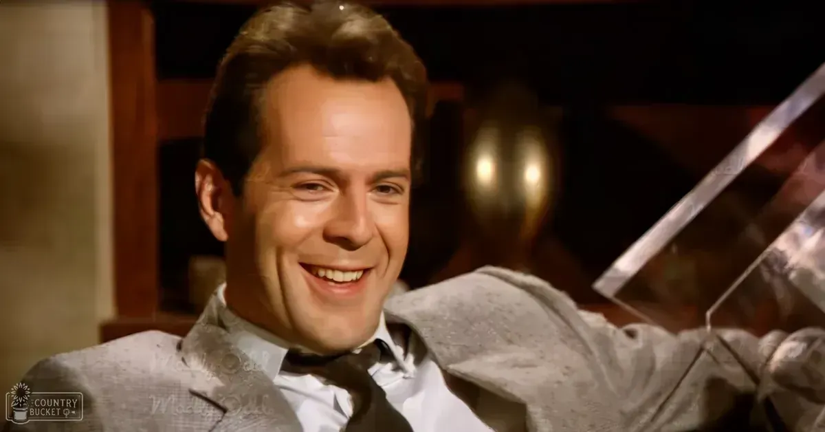 Adult male wearing a late 20th-century patterned suit jacket indoors with warm lighting and decorative elements.