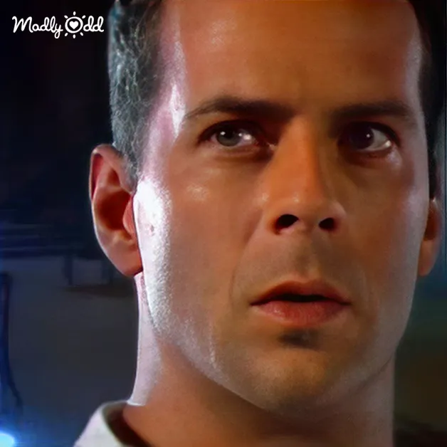 A middle-aged adult male in a dimly lit indoor setting, wearing a white shirt with a collar.