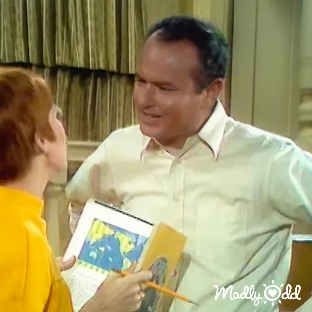 Middle-aged man in a light green button-up shirt and woman in a bright yellow dress indoors, with neutral-toned walls and natural lighting.