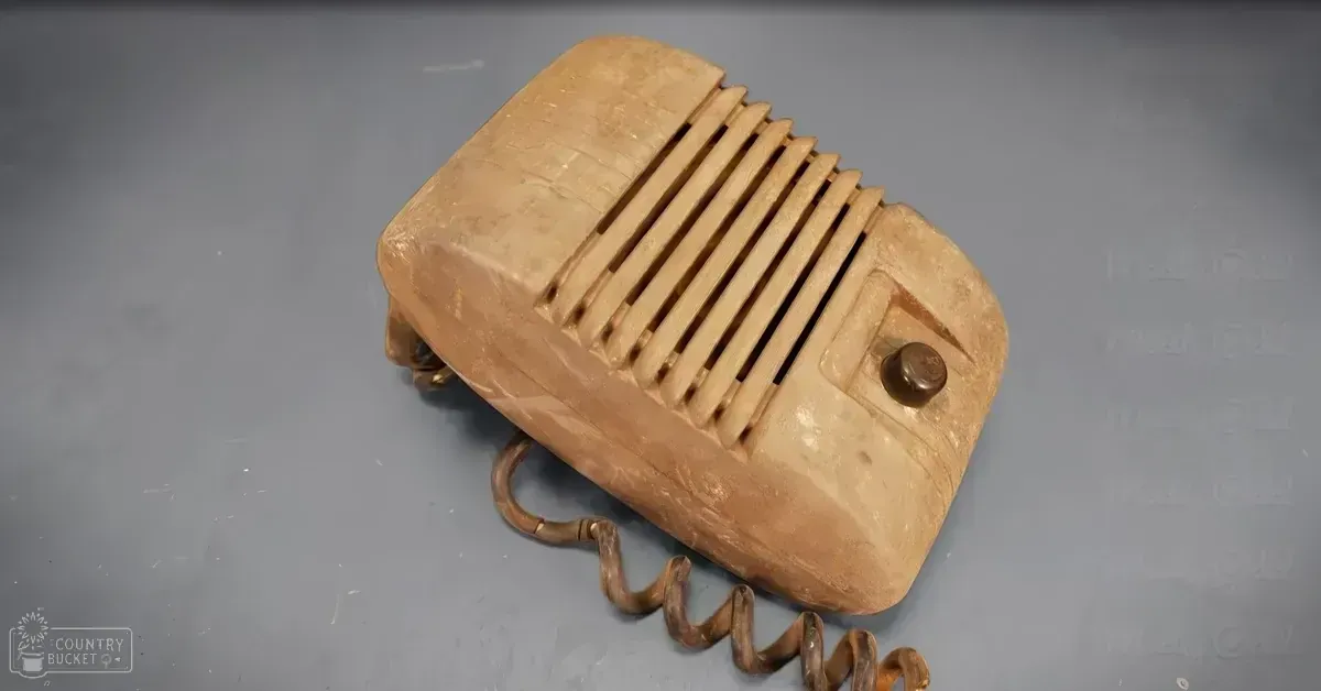 A vintage-style microphone with coiled cord and horizontal slits on its front panel in an indoor setting with even artificial lighting.
