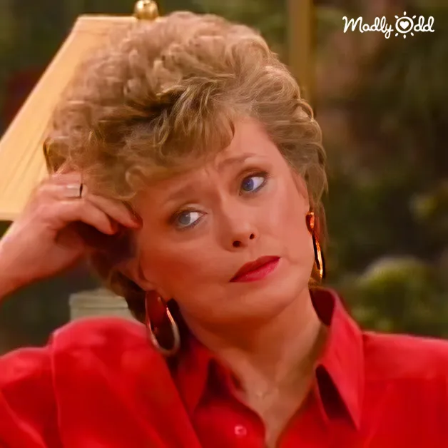 Middle-aged to older adult female in a red button-up shirt with smooth fabric, likely silk or satin, indoors with natural light and greenery.