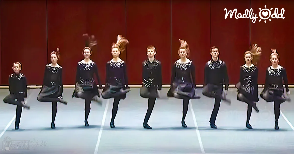 Group of young dancers performing in an indoor dance studio with red backdrop and artificial lighting.
