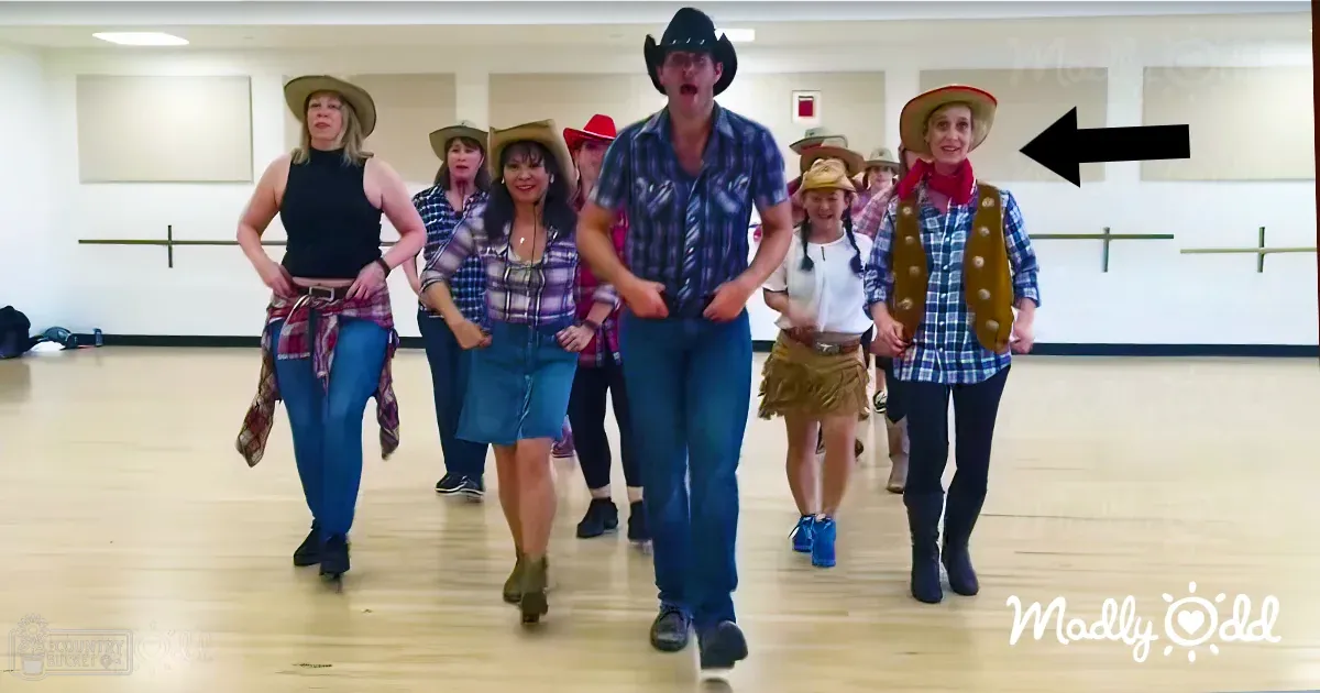 Adults participating in a dance class at an indoor studio, wearing casual attire with jeans and cowboy boots; wooden flooring, ballet barres along the walls.