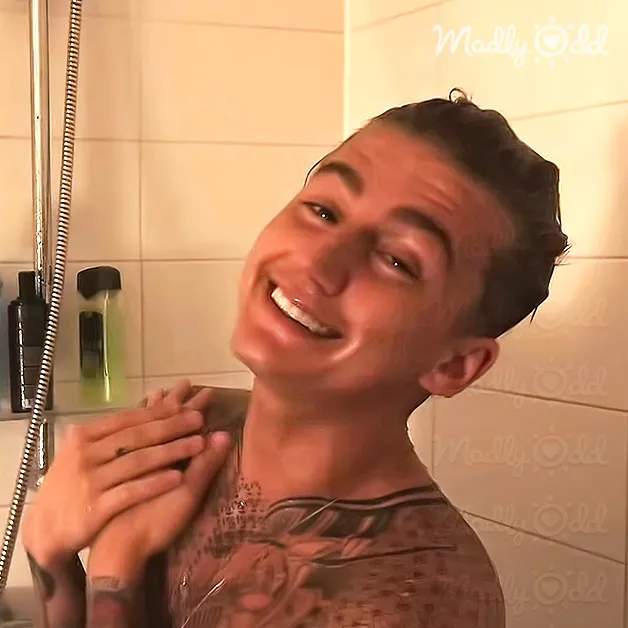 A young adult male wearing a brown and white patterned crew neck t-shirt with relaxed fit, standing in front of bathroom tiles with 'Madly Odd' logo.