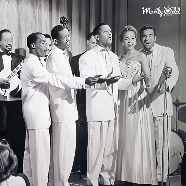 A mid-20th century musical performance group dressed formally on an indoor stage with microphones and a banjo in the background, suggesting a live concert or theater setting.