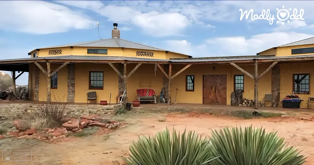 A rural home in a desert-like setting with outdoor furniture, potted plants, and firewood.