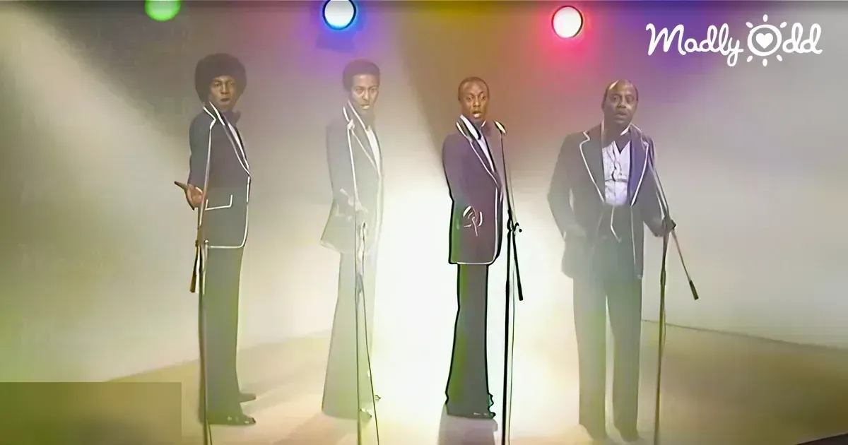 Young adult male singers in dark suits perform on a dramatic indoor stage under artificial lighting.