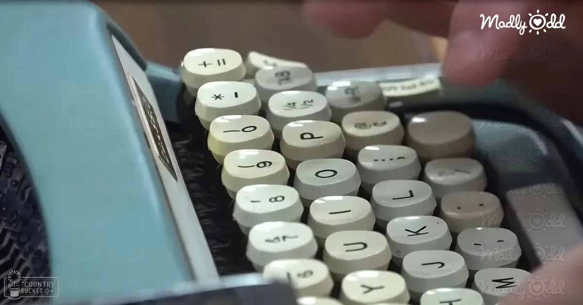 Close-up of an old-fashioned typewriter with white keys with letters and symbols, light blue casing on one side; indoors setting with neutral tones in the background.