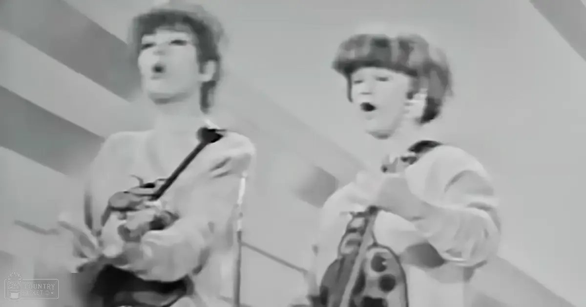 A musical performance scene with two young adult males in 1960s attire on a stage with a plain backdrop, no animals or other notable objects visible.