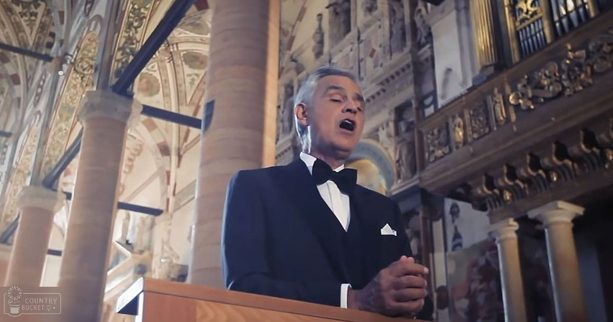 A middle-aged man in a dark tuxedo sings inside an ornate church with intricate architectural details.