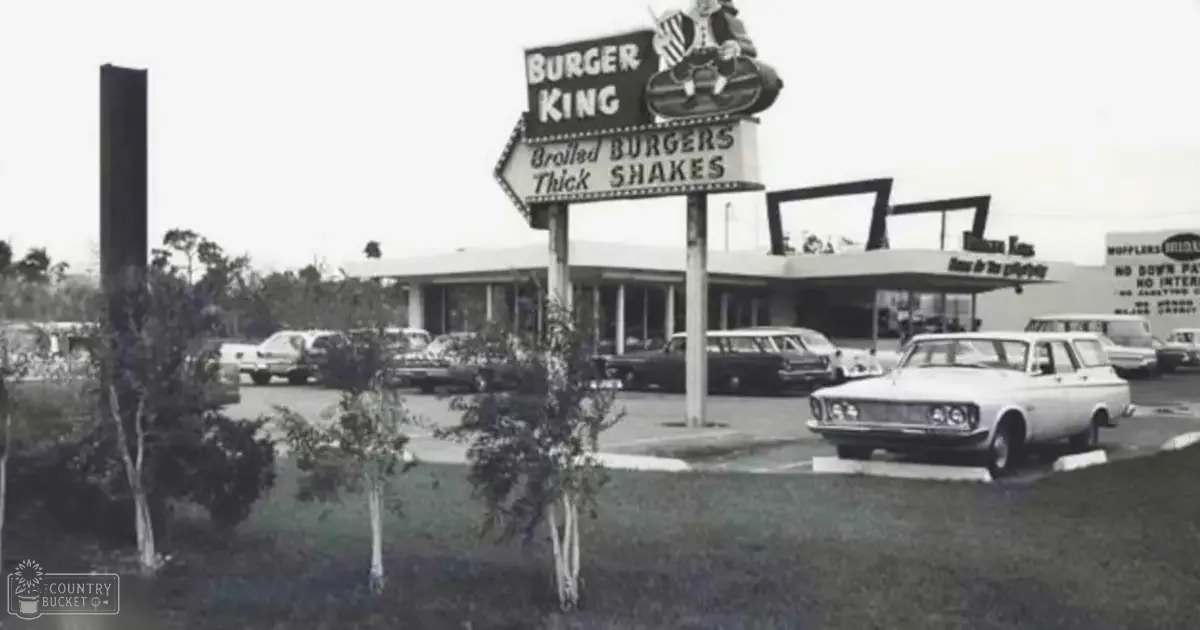 Burger King restaurant sign and vintage cars in a suburban outdoor setting during spring or summer with muted tones.