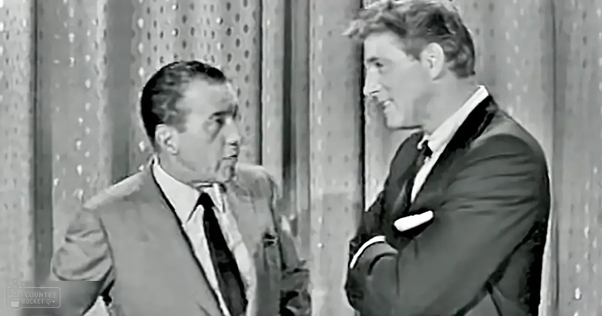 A mid-20th century comedic scene with two adult male singers dressed in dark suits, white shirts, and patterned ties against a perforated studio backdrop.