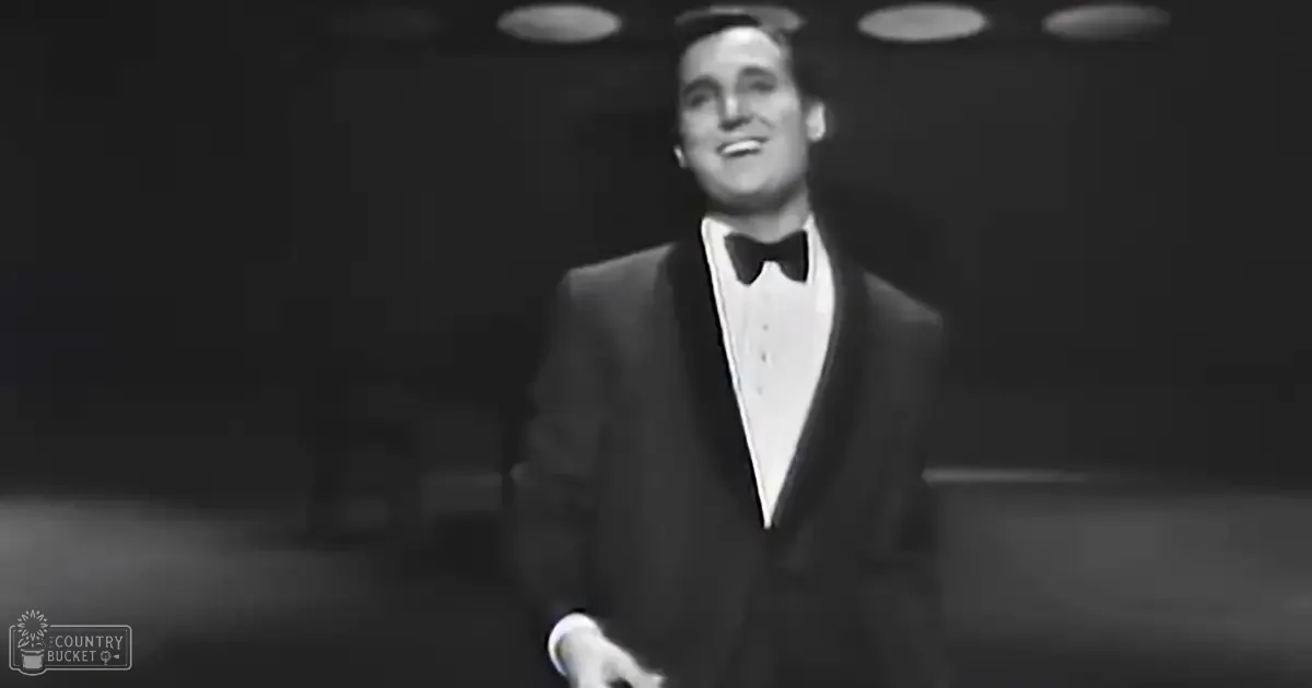 A middle-aged man wearing a formal suit with a bow tie, standing indoors at what appears to be a performance venue.