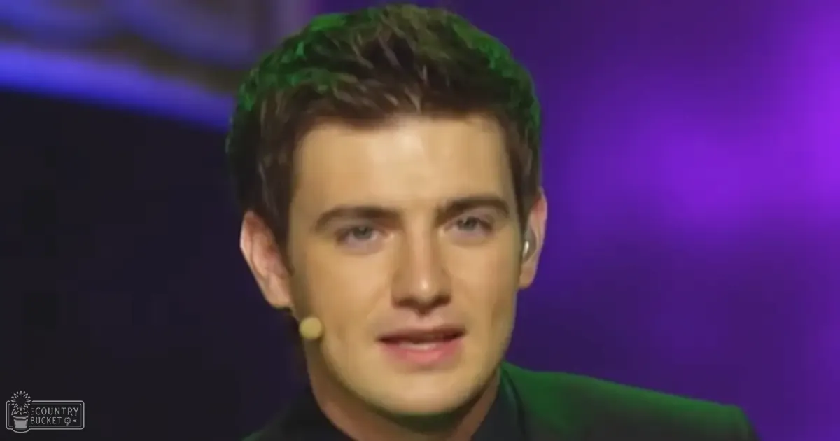 Young adult male in a tailored dark green suit jacket with high collar and lapel, set against purple and blue studio lighting.