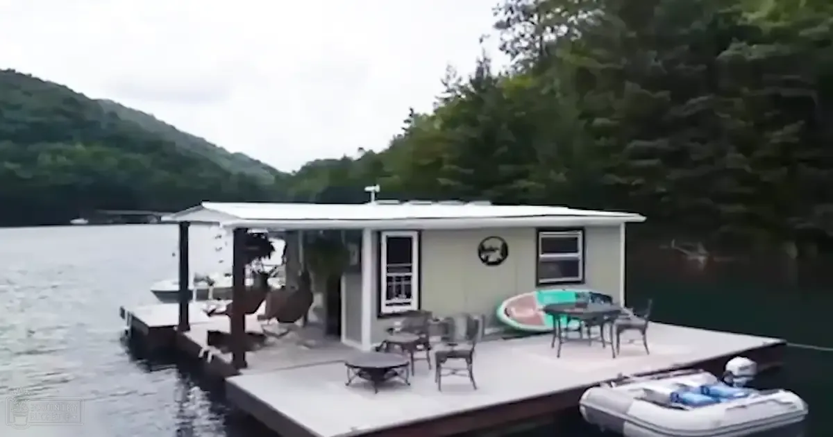 A serene lakeside scene with a houseboat, outdoor furniture, and greenery under diffused daylight.