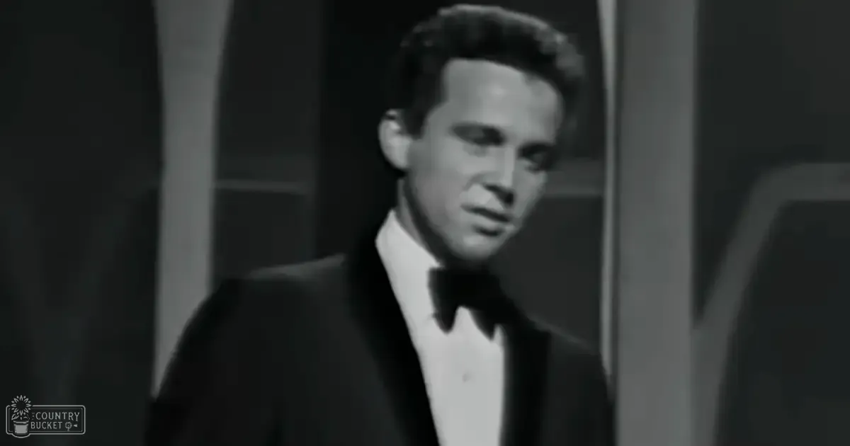 A young adult male wearing a formal black tuxedo with a bow tie, indoors in an evening setting.