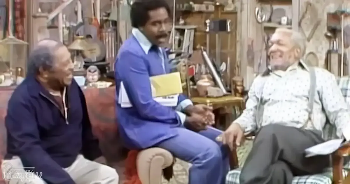 An old-fashioned living room with adults seated in a sitcom setting; furniture includes couches and book-filled shelves.