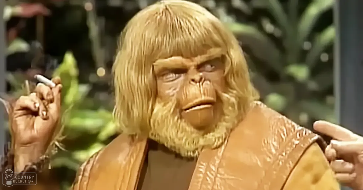 A person dressed as a character from 'Planet of the Apes' stands among indoor plants, holding a cigarette in an environment that suggests daytime with greenery.