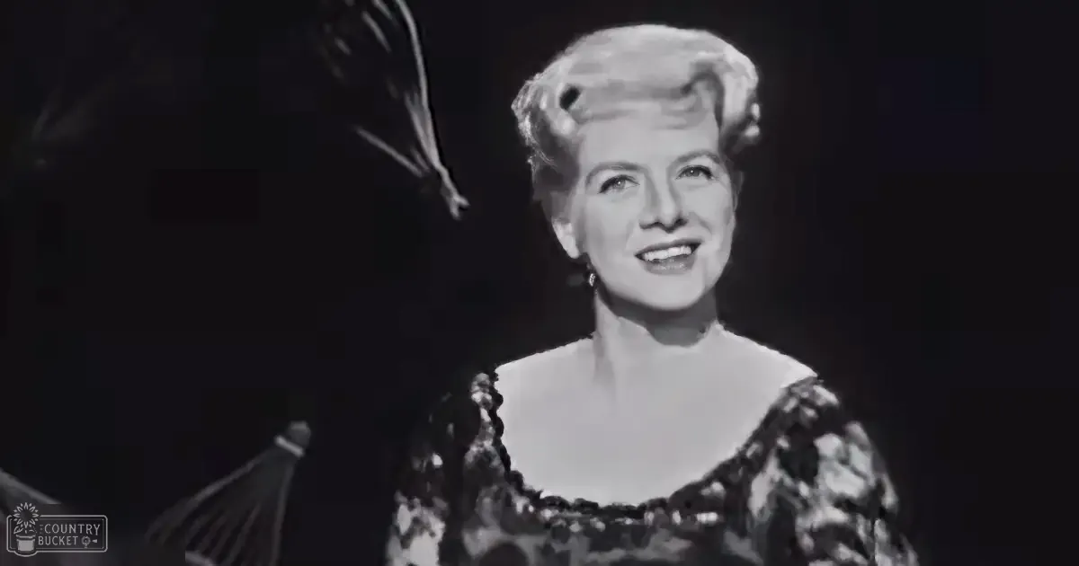 A middle-aged adult female wearing an elegant evening gown with intricate detailing, standing indoors under dark lighting typical of a stage or performance venue.