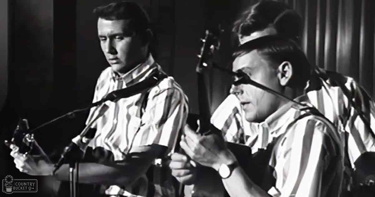 Musical performance scene with two young adult male singers wearing striped shirts, microphones held by each, curtains suggesting indoor stage setting from mid-20th century.