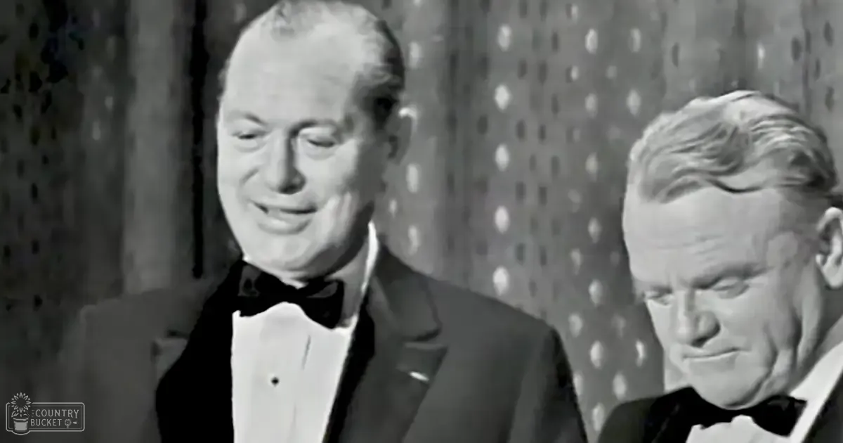 Two adult males, likely middle-aged and older adults, wearing black tuxedos with white shirts and bow ties, set against a patterned indoor backdrop suggesting a formal gathering.
