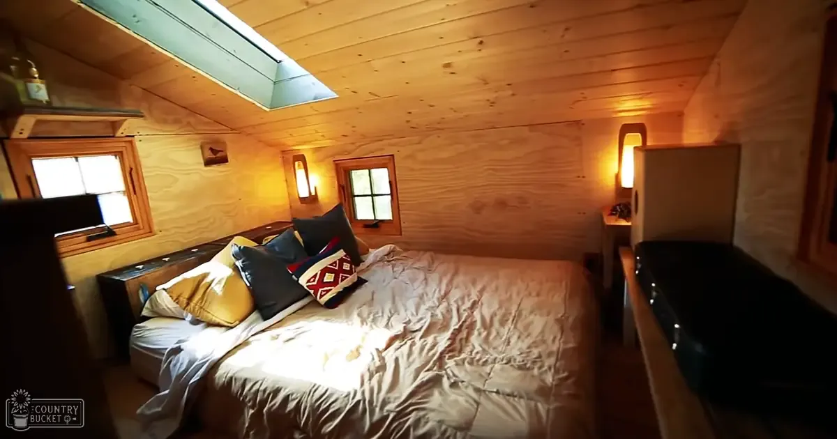 Cozy bedroom scene in a tiny house or cabin with sunlight streaming through windows.