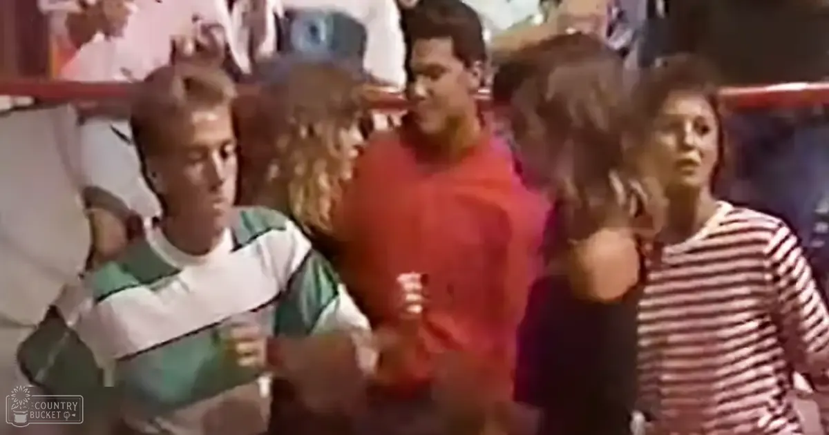 A group of individuals gathered indoors, wearing casual attire. A young adult male in a green and white striped shirt stands on the left; an adult female with a striped shirt is to his right.