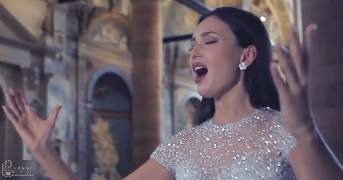 A young adult female singing amidst ornate indoor architectural details with natural light streaming through.