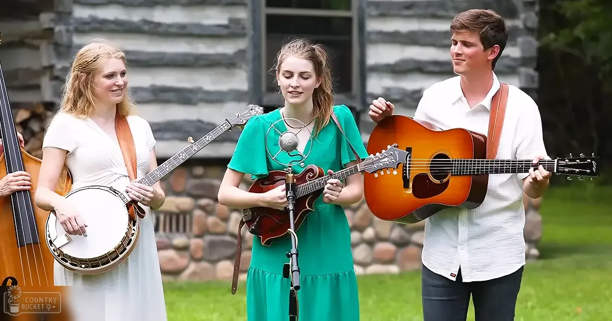 Musical performance in an outdoor setting with stone cabin, grassy ground, and natural light.