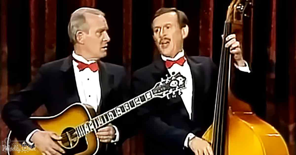 Adult male musicians performing with guitars and a double bass on stage under dim lighting.
