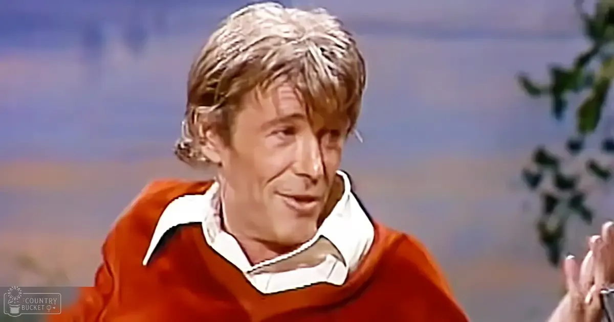A middle-aged man wearing a red V-neck sweater with white collars in an indoor setting under artificial lighting.