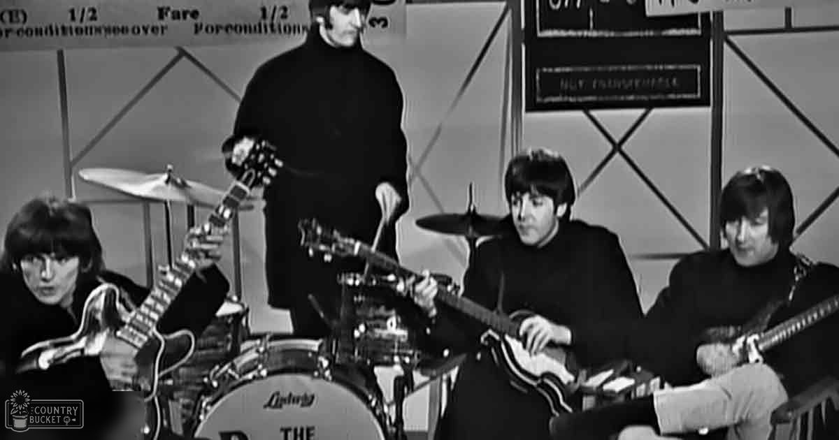 A musical performance scene with four adult males wearing dark turtleneck sweaters, set indoors on a stage with framed text backdrop and visible Ludwig drum branding.