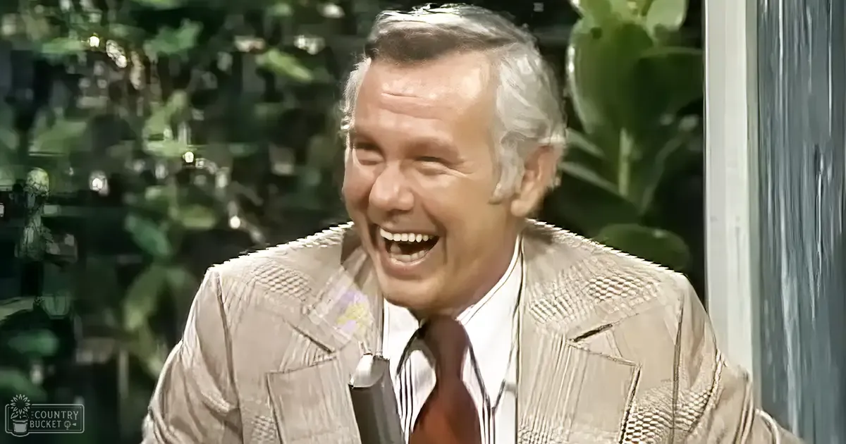 An older adult male wearing a textured, light-colored jacket and a white collared shirt with vertical stripes, standing outdoors in a lush green garden on what appears to be a bright midday spring or summer day.