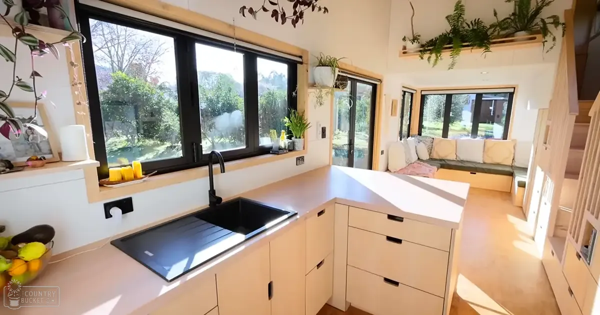 An indoor home kitchen with modern appliances, plants, and a view of greenery through the windows during daytime in spring or summer.