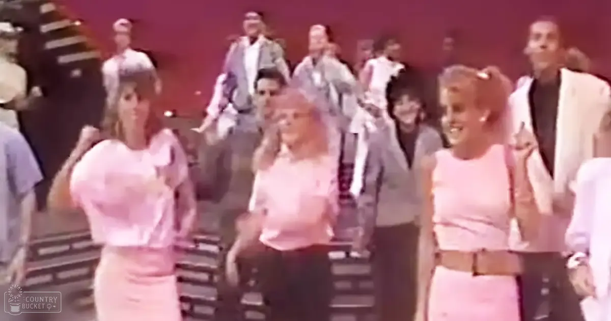 Young adults in dance performance setting, bright indoor lighting, pink and white attire.