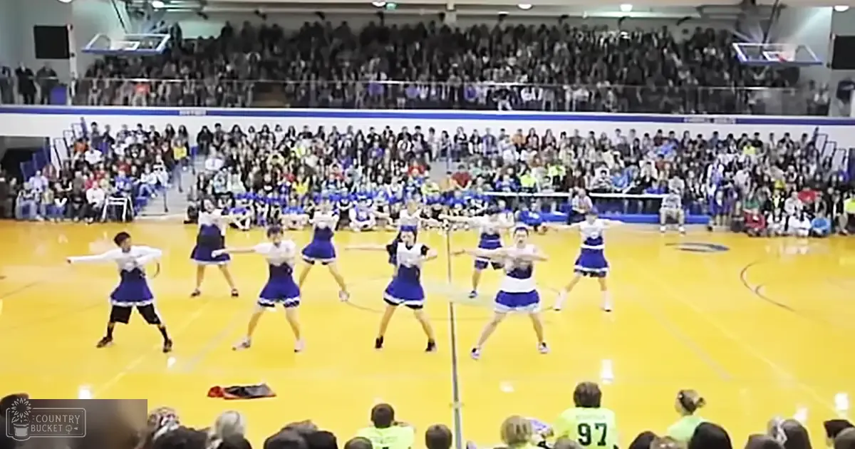 A cheerleading routine takes place in an indoor sports arena filled with spectators at night.