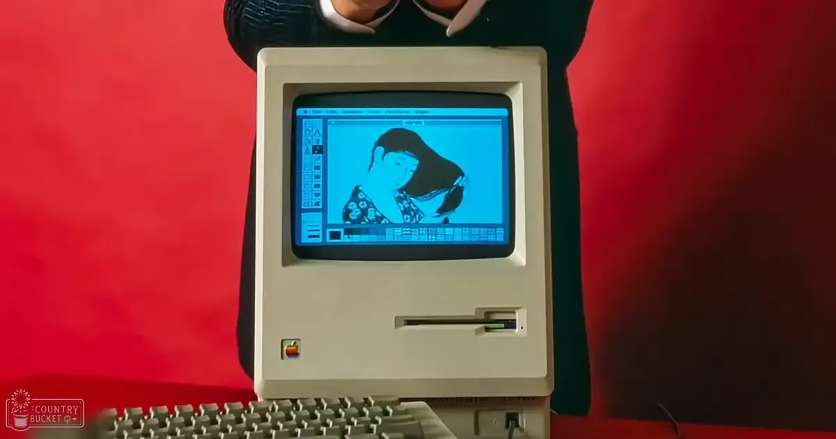 A vintage Apple computer with a digital drawing of a figure against a blue background, set in a studio environment with even bright lighting and red backdrop.