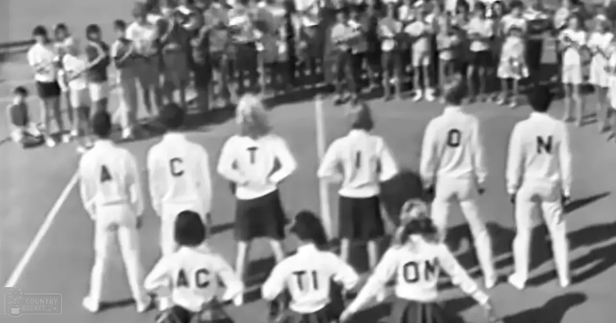 Children in white sweaters with 'A', 'C', 'T', 'I', 'O', 'N' letters, participating in an outdoor event on bleachers during bright daylight.