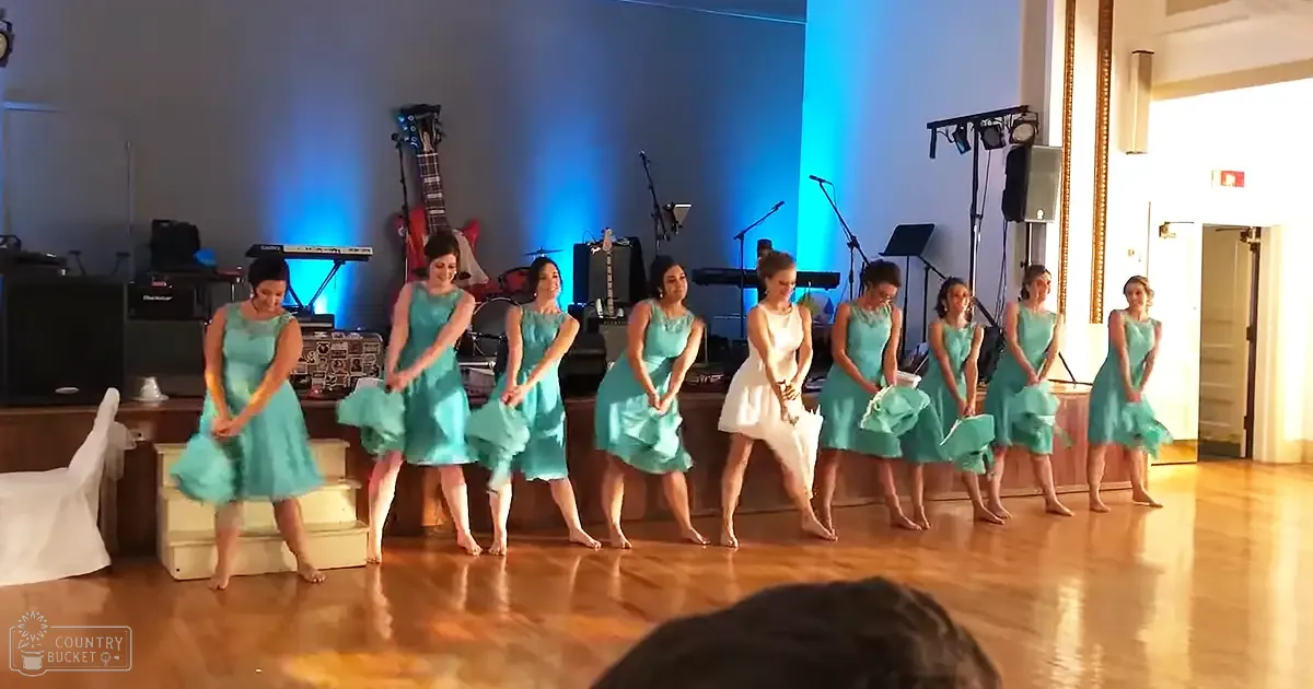 Young adult female performers in turquoise dresses with ruffled skirts, performing indoors near musical instruments under stage lighting.